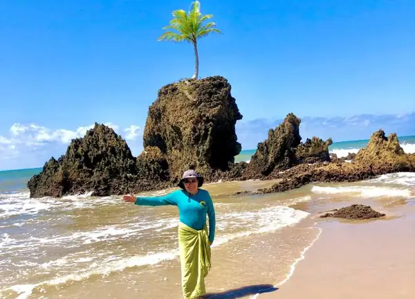 Cliente em praia com piscinas naturais e coqueiro na pedra